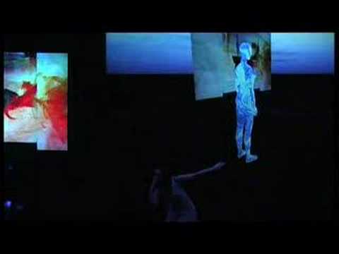 A dancer on a dark stage with projected video