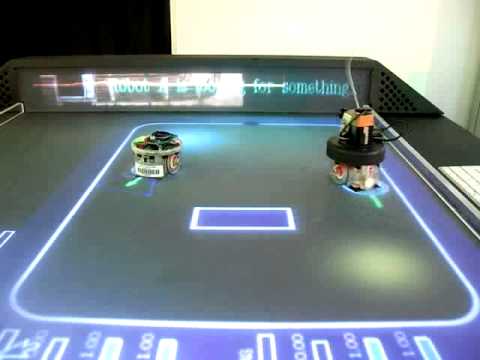 Two small robots on a lit arena table